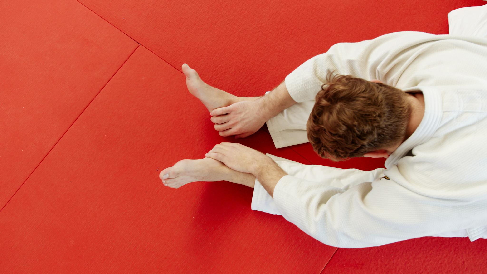 Martial artist in uniform stretching on a vibrant red mat during training session.