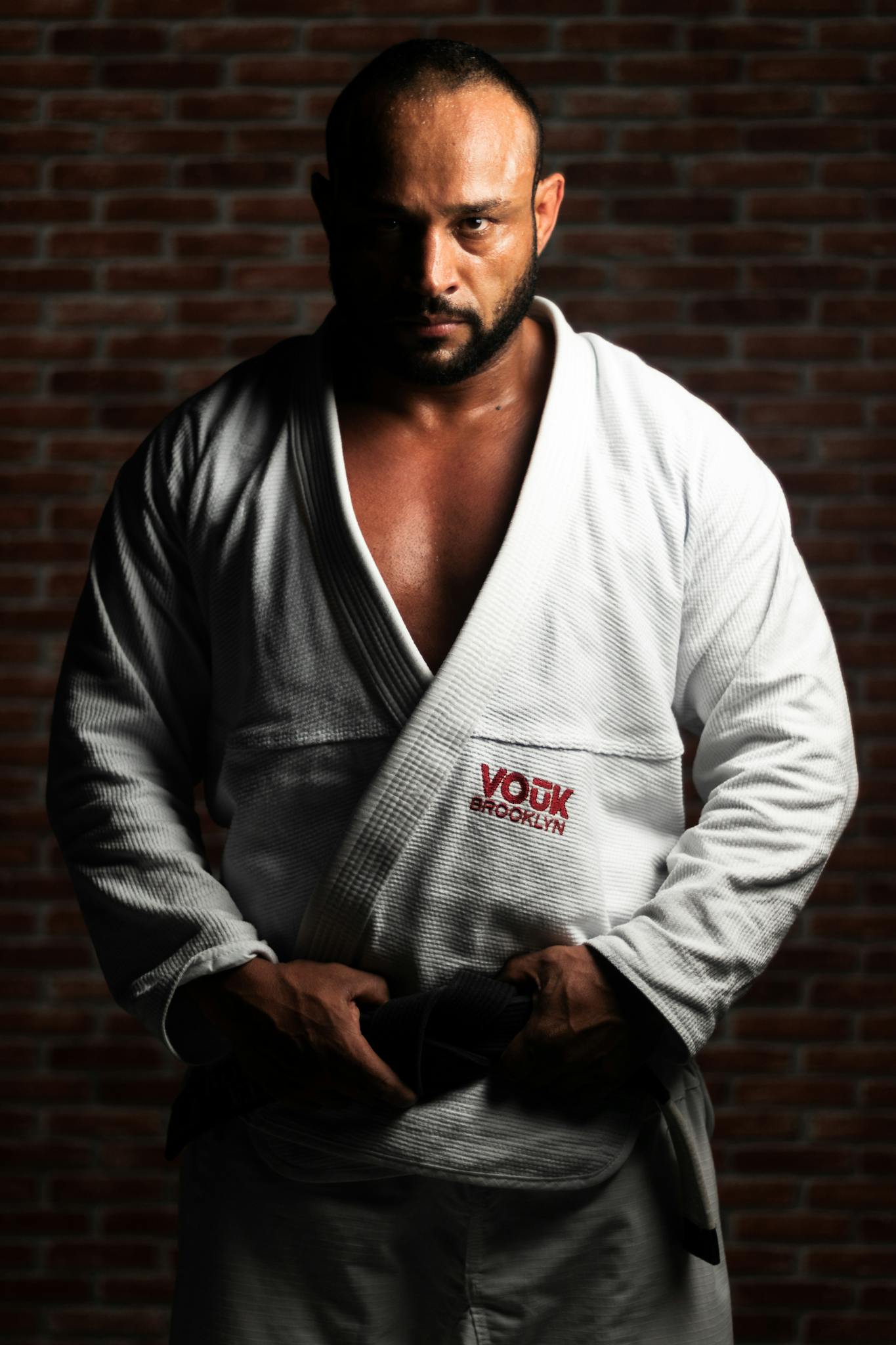 Strong Brazilian jiu-jitsu athlete in traditional gi against a brick wall backdrop.